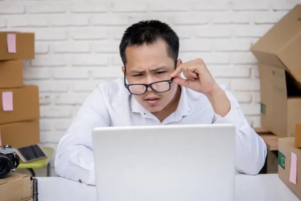 A confused business owner looking at his computer, adjusting his glasses.